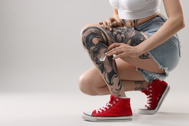 Photo of Woman applying healing cream onto her tattoos against light background, closeup. Space for text