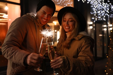 Photo of Happy couple with sparklers and glasses of champagne at winter fair