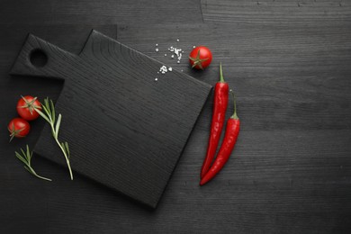 Photo of Cutting board, rosemary, chili peppers and tomatoes on black wooden table, flat lay. Space for text