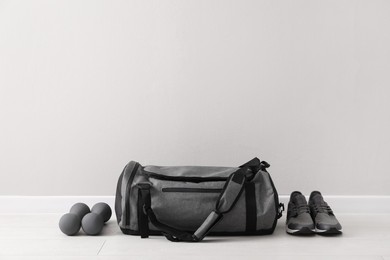 Grey sports bag, sneakers and dumbbells on floor near light wall, space for text