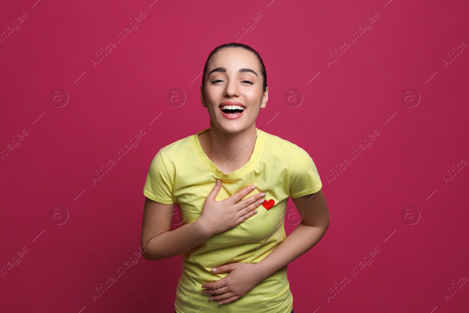 Photo of Beautiful young woman laughing on maroon background. Funny joke