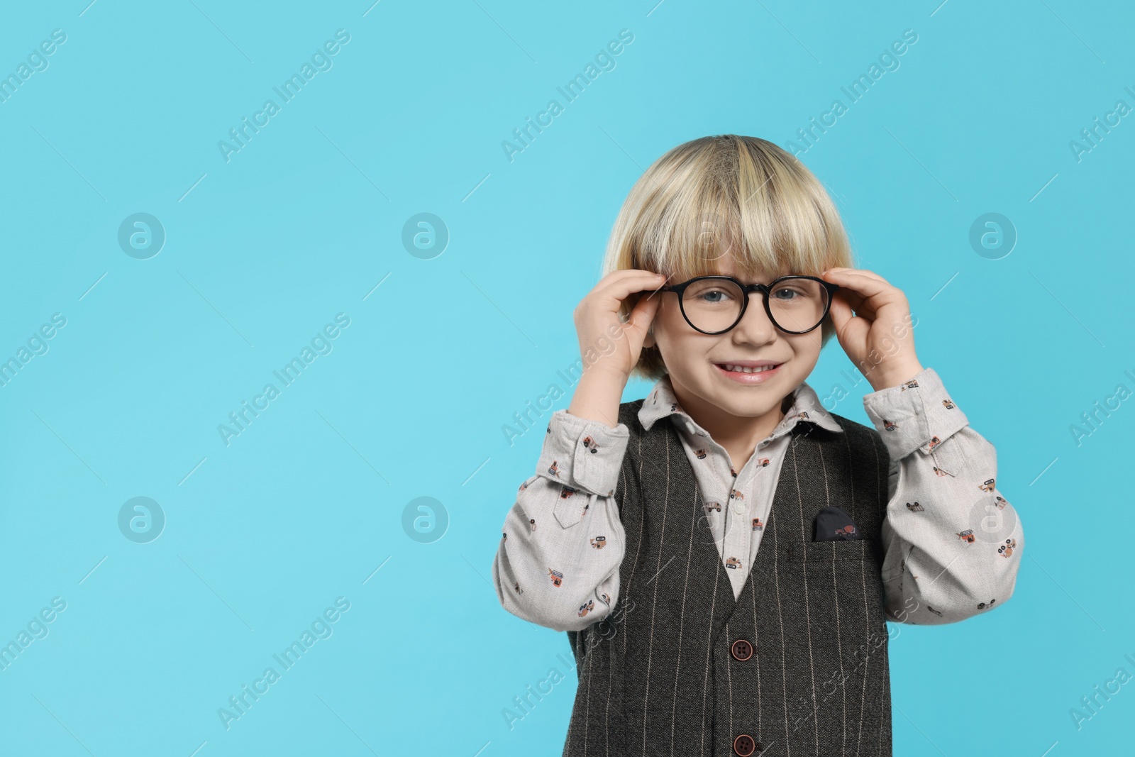 Photo of Cute little boy wearing glasses on light blue background, space for text