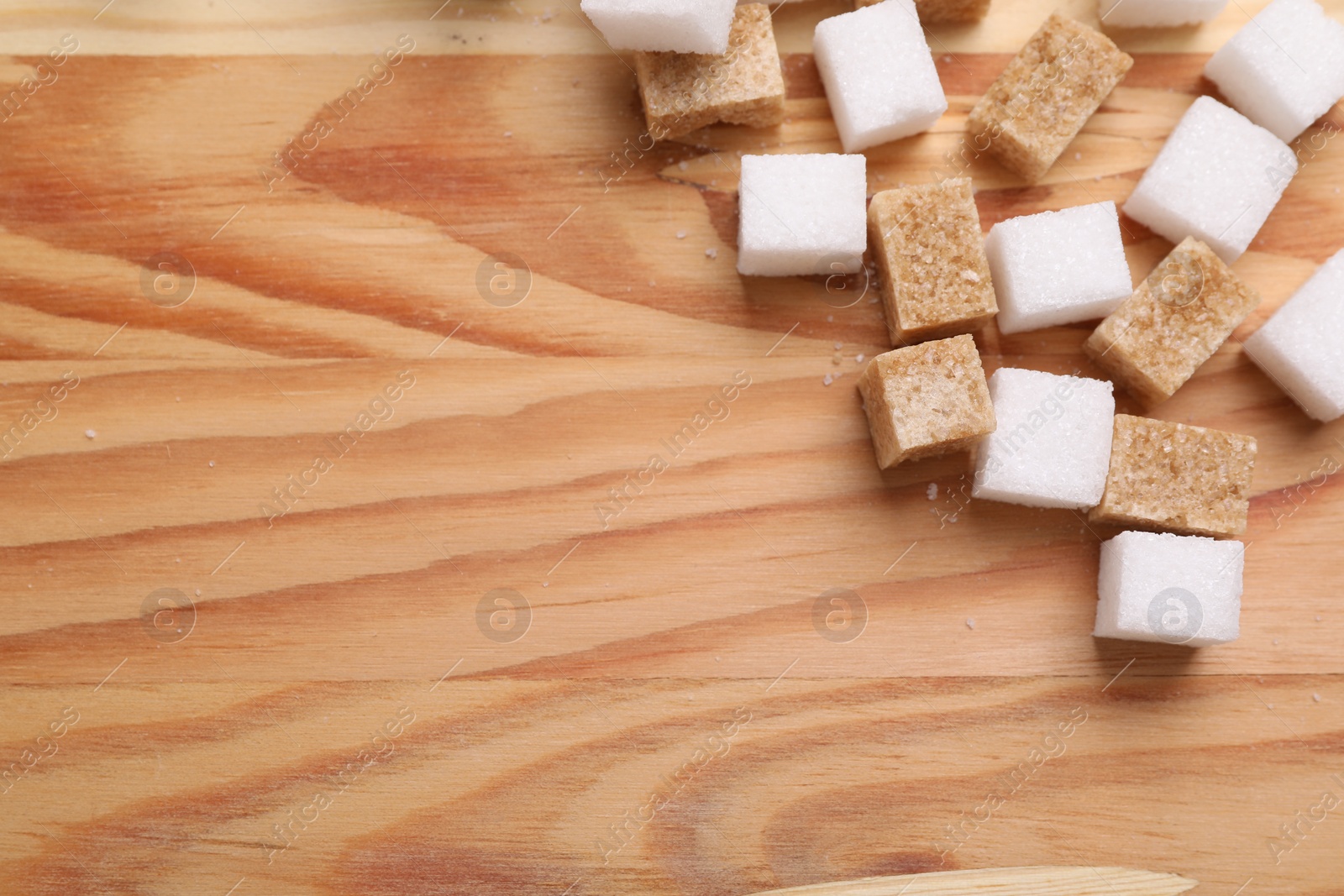 Photo of White and brown sugar cubes on wooden table, flat lay. Space for text