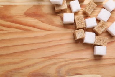 Photo of White and brown sugar cubes on wooden table, flat lay. Space for text