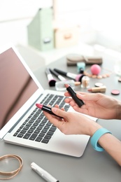 Photo of Young woman with makeup products using laptop at table. Beauty blogger