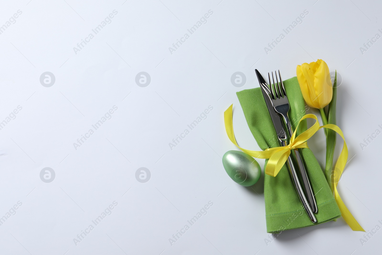 Photo of Cutlery set, Easter egg and tulip on white background, top view with space for text. Festive table setting