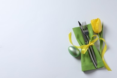 Photo of Cutlery set, Easter egg and tulip on white background, top view with space for text. Festive table setting