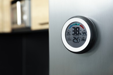 Round digital hygrometer with thermometer on fridge in kitchen. Space for text