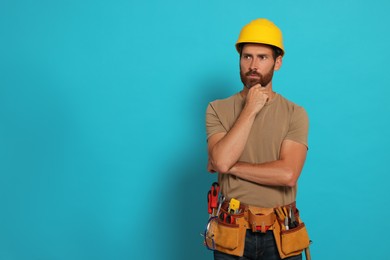 Photo of Professional builder in hard hat with tool belt on light blue background, space for text