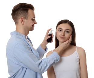 Photo of Man spraying medication into woman`s ear on white background