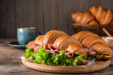 Tasty croissant sandwiches with ham on wooden table, closeup