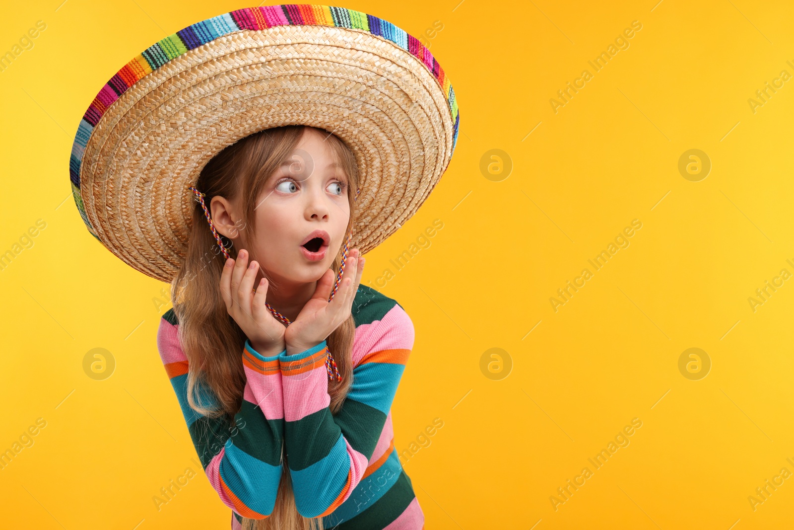 Photo of Emotional girl in Mexican sombrero hat on orange background. Space for text