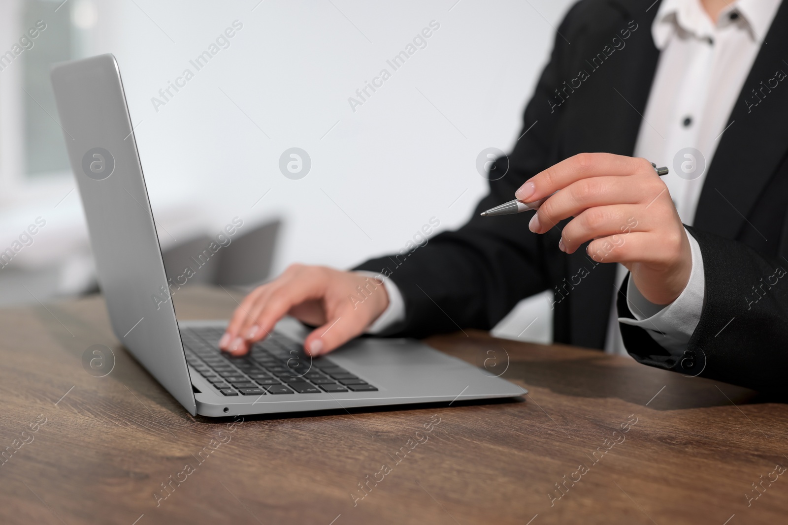 Photo of Woman with pen working on laptop at wooden table, closeup. Electronic document management