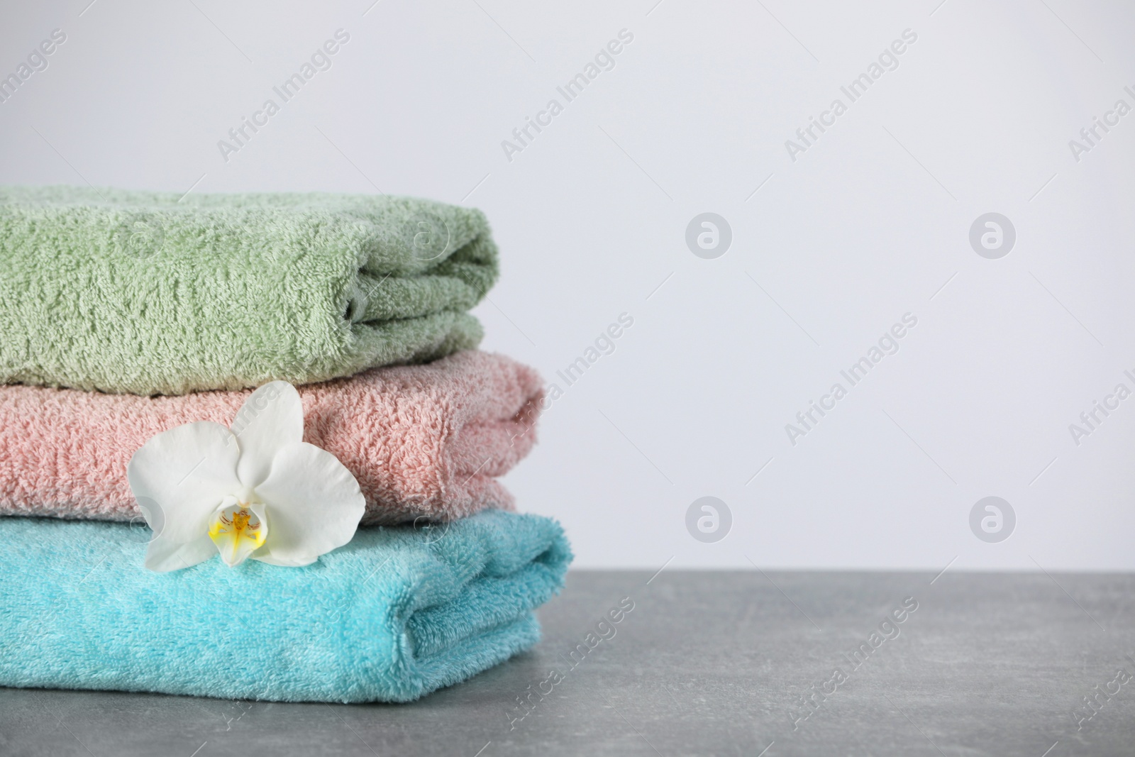 Photo of Stacked soft colorful towels with flower on grey table, space for text