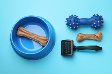 Photo of Bowl, dog treat, toy and brush for pet on light blue background, flat lay