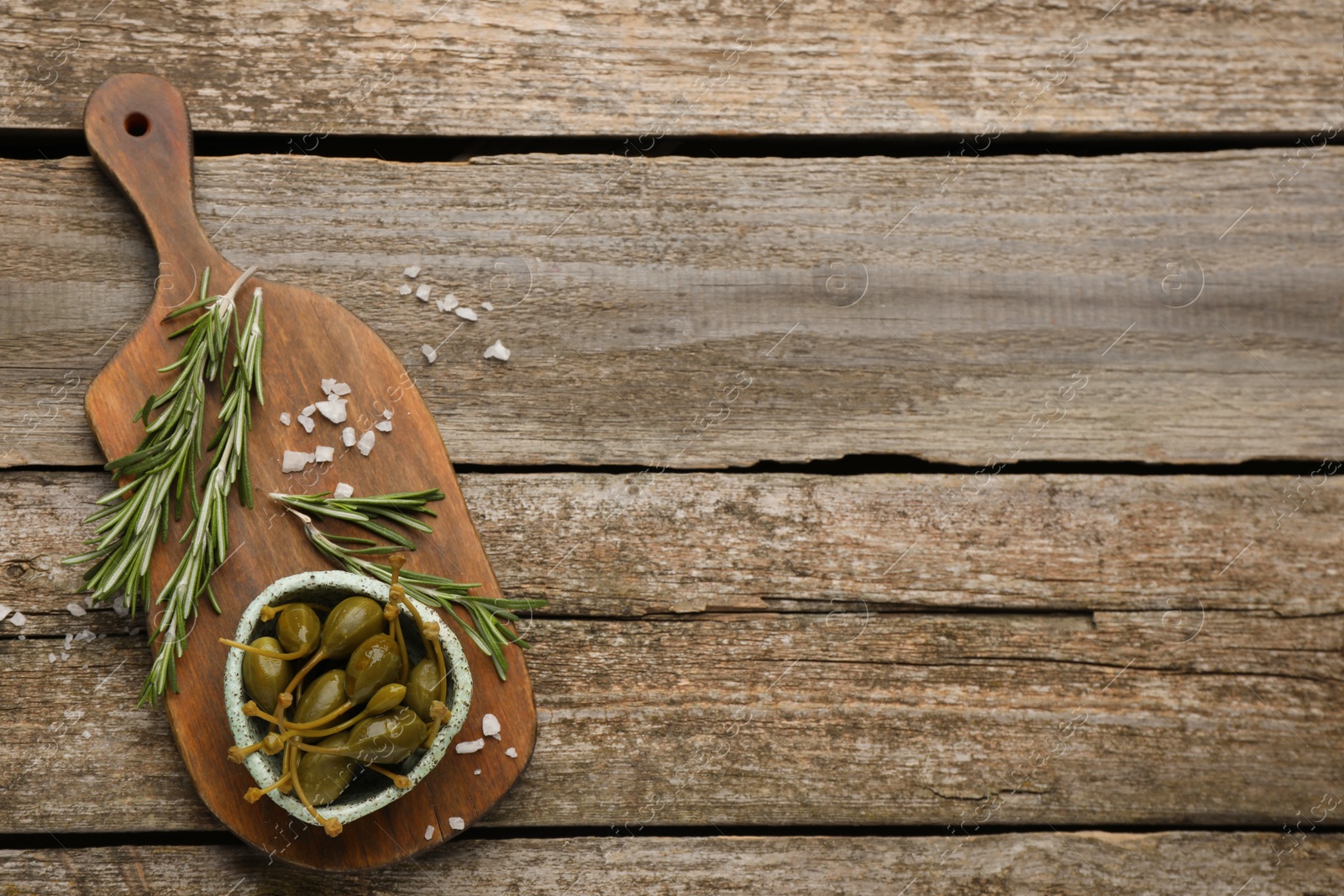 Photo of Delicious pickled capers and rosemary twigs on wooden table, top view. Space for text