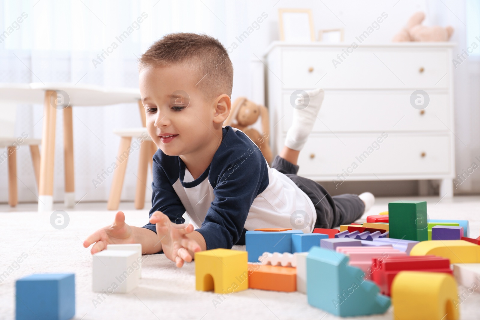 Photo of Cute little boy playing with colorful building blocks on floor in room