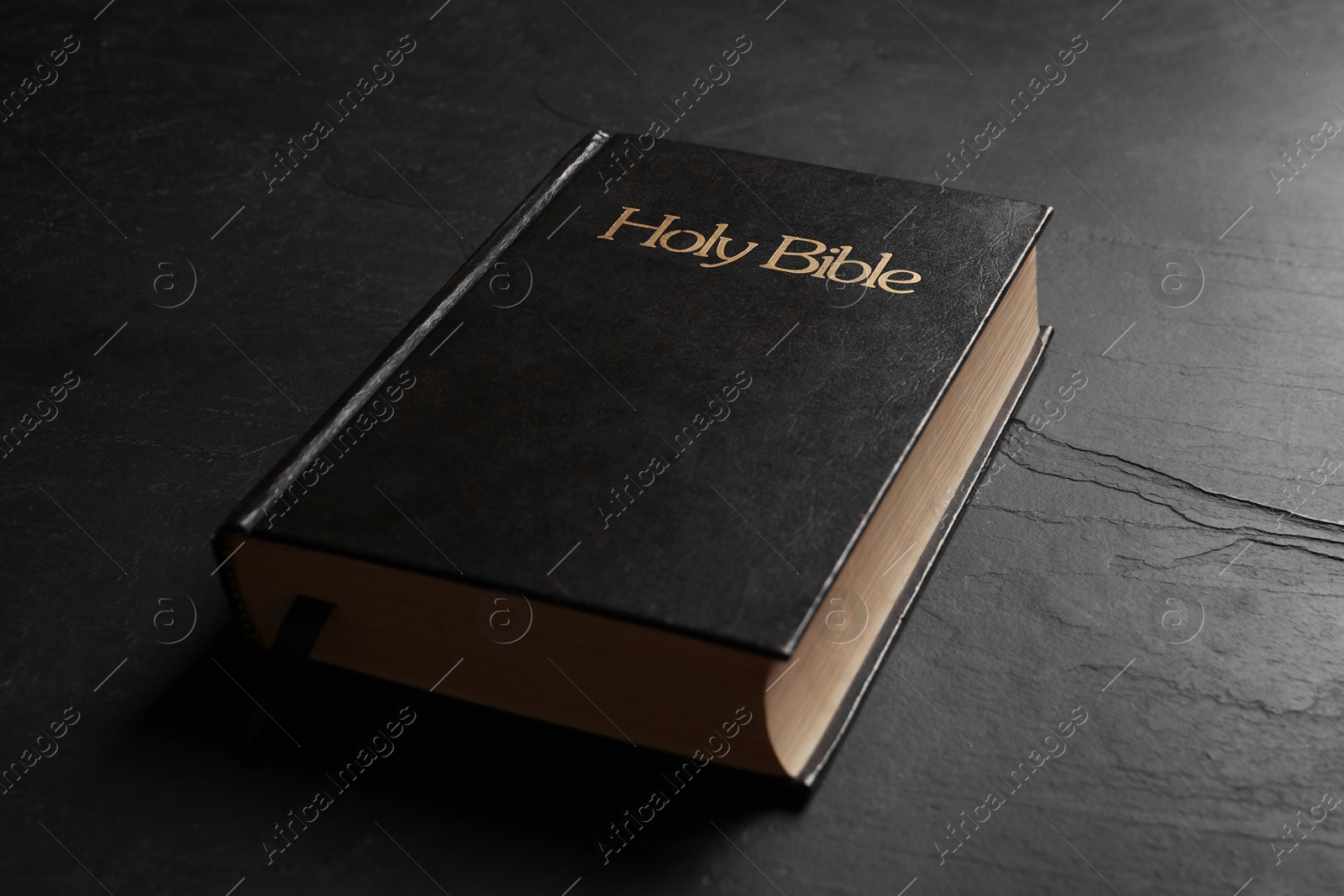 Photo of Hardcover Bible on black table, closeup. Religious book