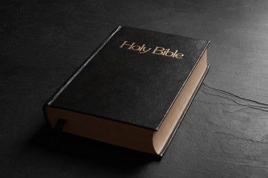 Photo of Hardcover Bible on black table, closeup. Religious book