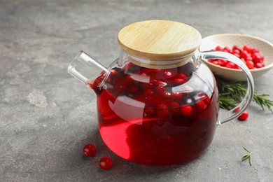 Photo of Tasty hot cranberry tea in teapot and fresh berries on light grey textured table