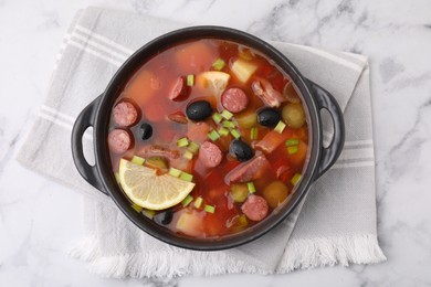 Photo of Meat solyanka soup with thin dry smoked sausages in bowl on white marble table, top view