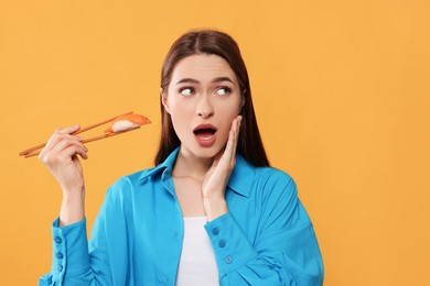 Emotional young woman holding sushi with chopsticks on orange background