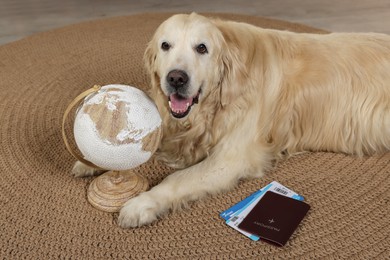 Photo of Cute golden retriever lying near passport, tickets and globe on floor at home. Travelling with pet