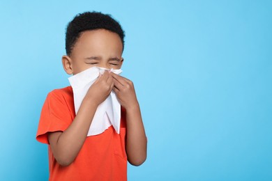 Photo of African-American boy blowing nose in tissue on turquoise background, space for text. Cold symptoms