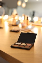 Eyeshadow palette and other cosmetic products on wooden dressing table in makeup room
