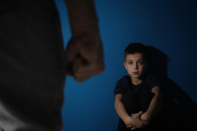 Man threatens his son on blue background. Domestic violence concept