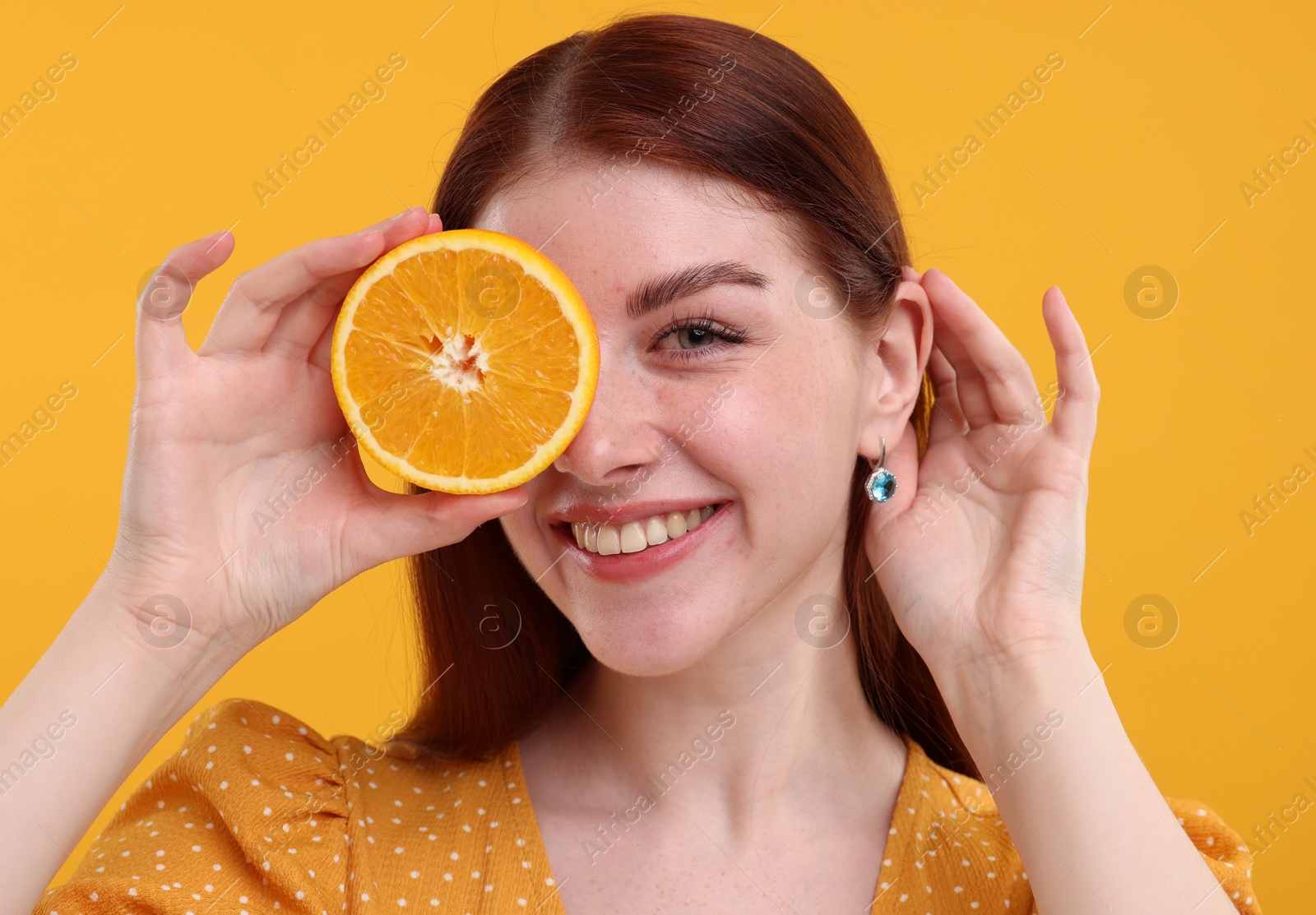 Photo of Smiling woman covering eye with half of orange on yellow background