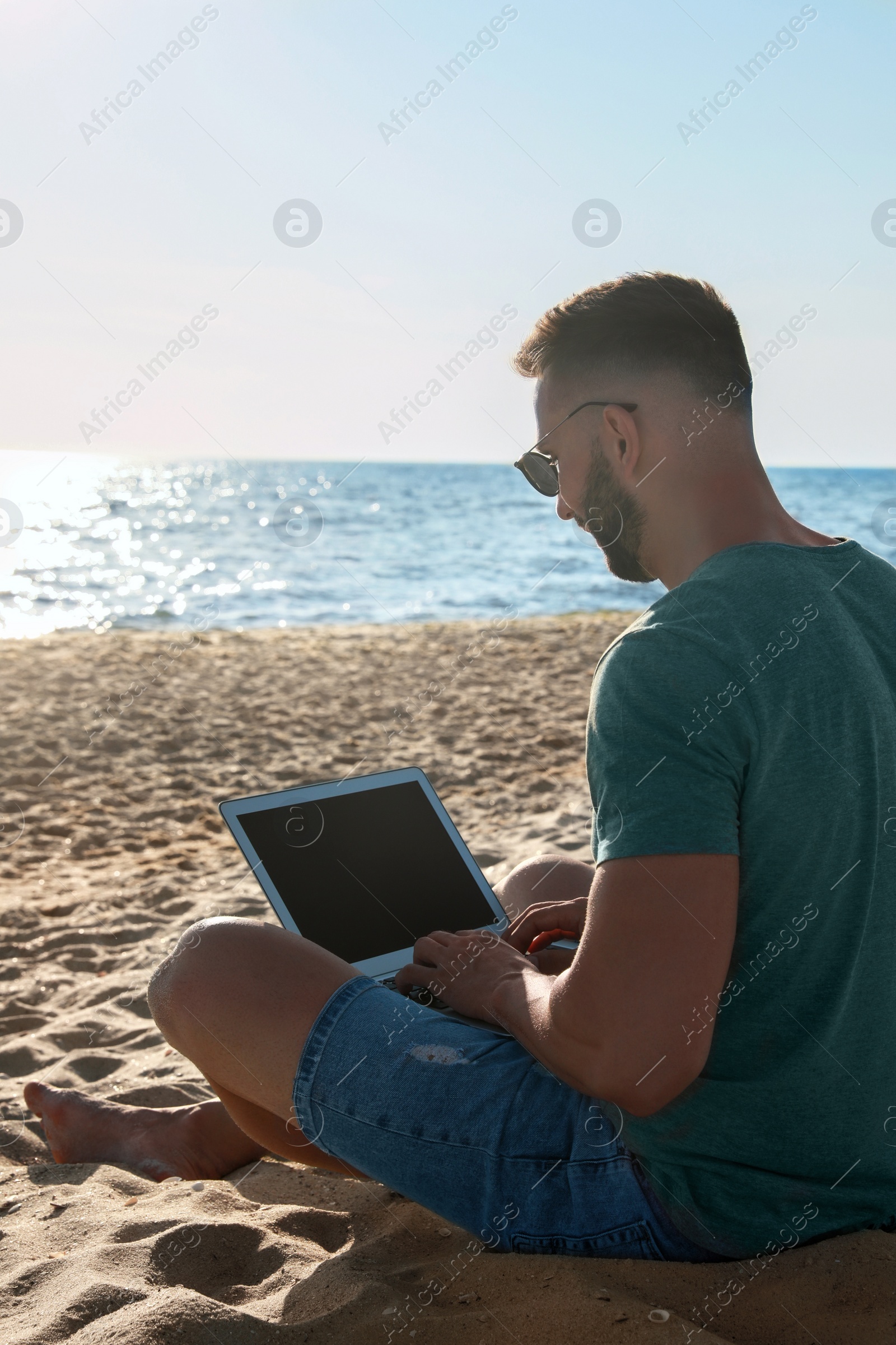 Photo of Man working with modern laptop on beach