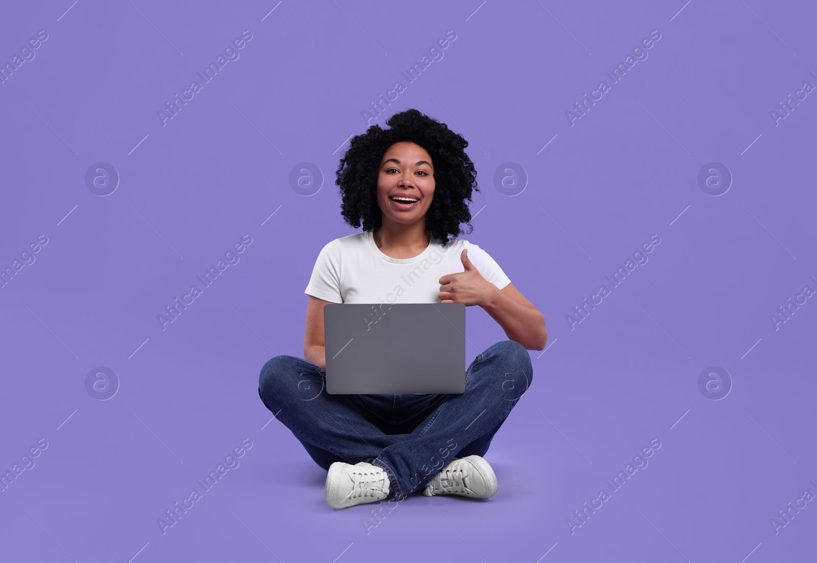 Photo of Happy young woman with laptop showing thumb up on purple background