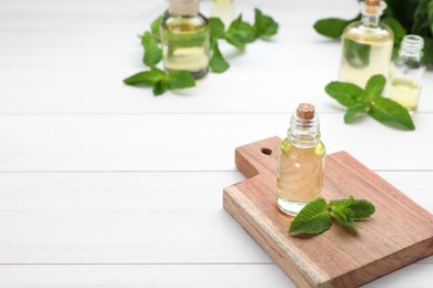 Bottle of essential oil and mint on white wooden table. Space for text