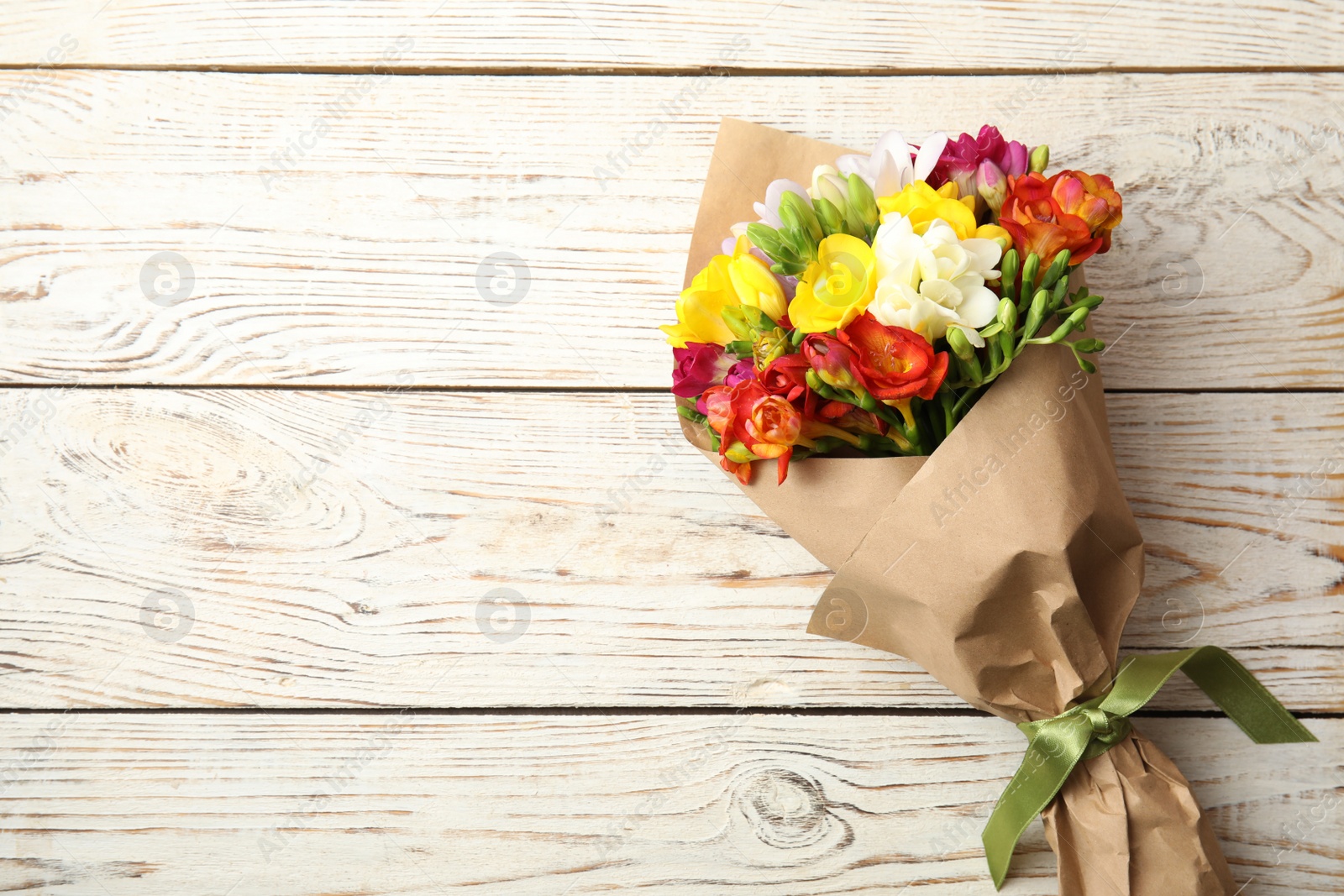 Photo of Bouquet of beautiful spring freesia flowers on wooden background, top view. Space for text