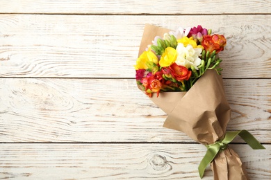 Photo of Bouquet of beautiful spring freesia flowers on wooden background, top view. Space for text