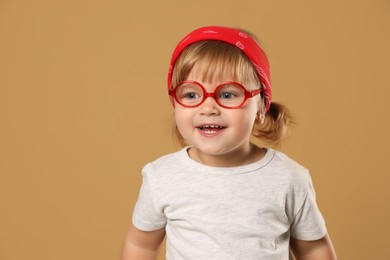 Photo of Cute little girl in glasses on pale brown background. Space for text