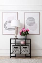 Photo of Console table with beautiful hydrangea flower and lamp near white wall in hallway. Interior design