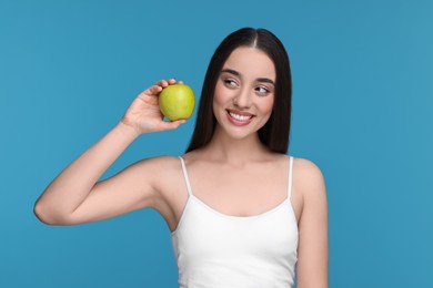 Beautiful young woman with apple on light blue background