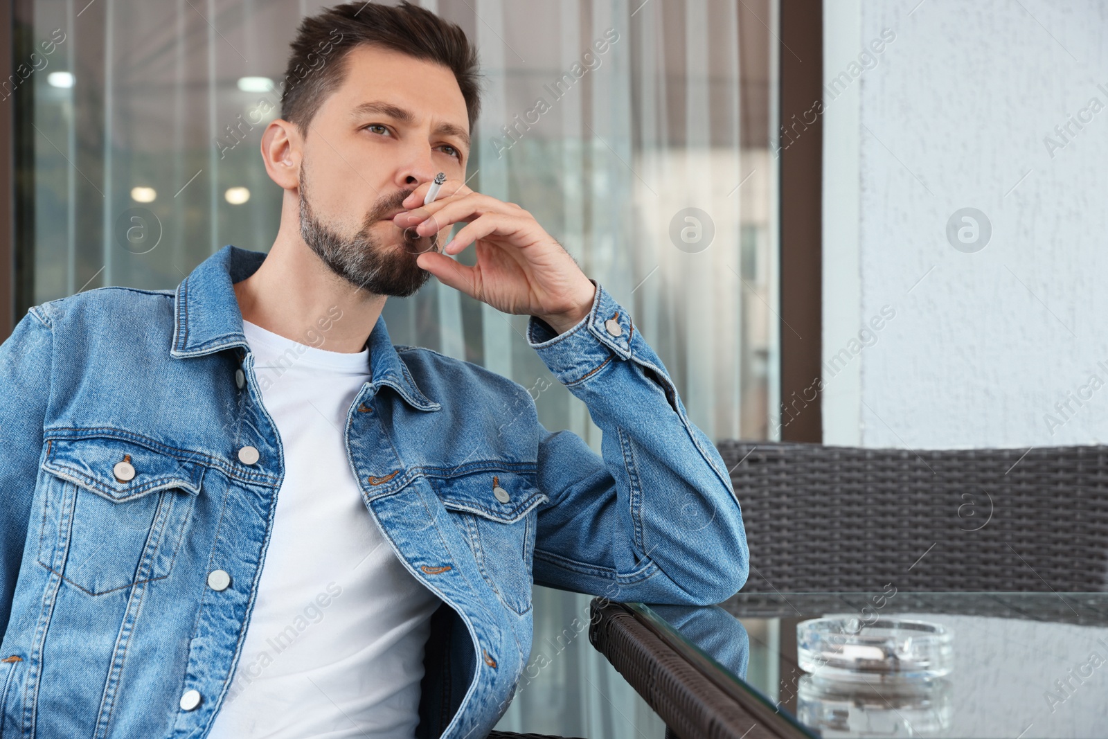 Photo of Handsome man smoking cigarette at table in outdoor cafe