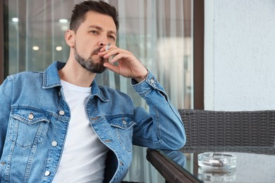 Photo of Handsome man smoking cigarette at table in outdoor cafe