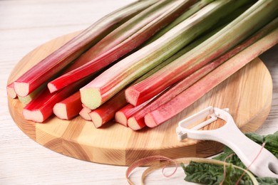 Photo of Cut fresh rhubarb stalks and peeler on white wooden table, closeup
