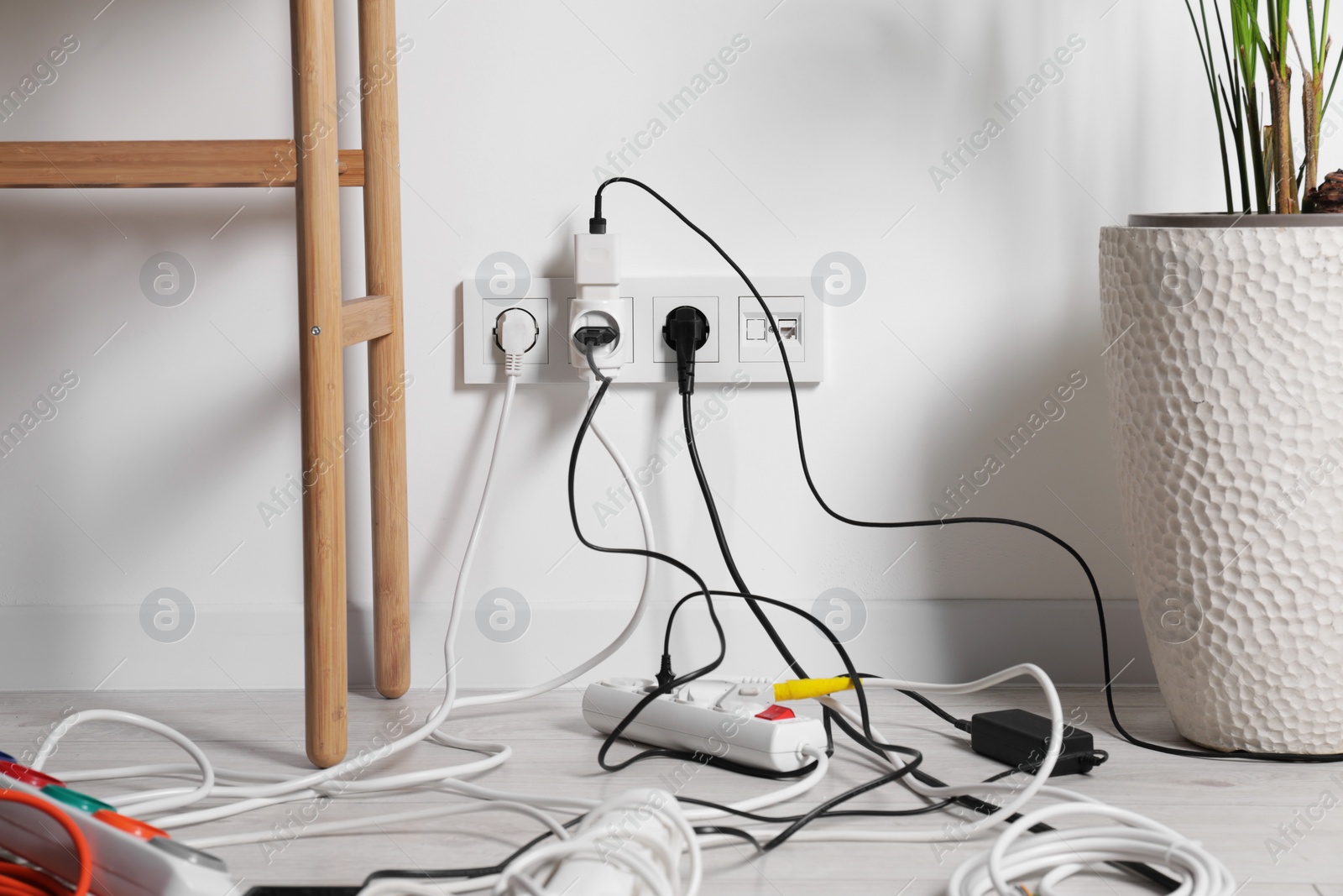 Photo of Different electrical plugs in socket and power strip on floor indoors