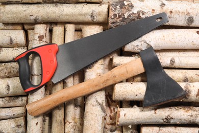 Photo of Saw with colorful handle and axe on firewood, flat lay