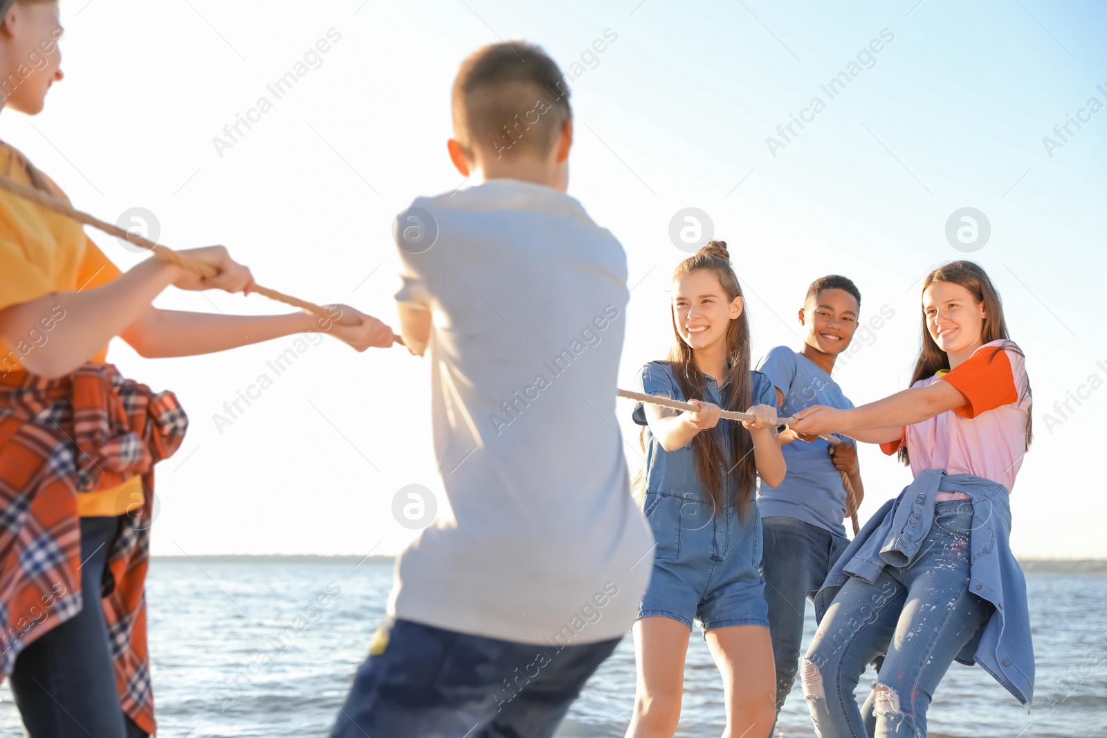 Photo of Group of children pulling rope during tug of war game on beach. Summer camp