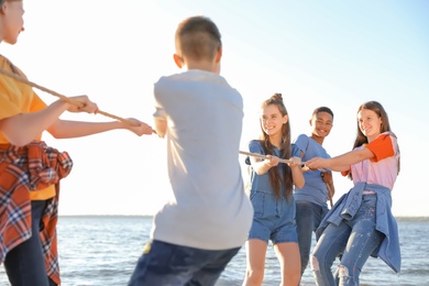 Photo of Group of children pulling rope during tug of war game on beach. Summer camp