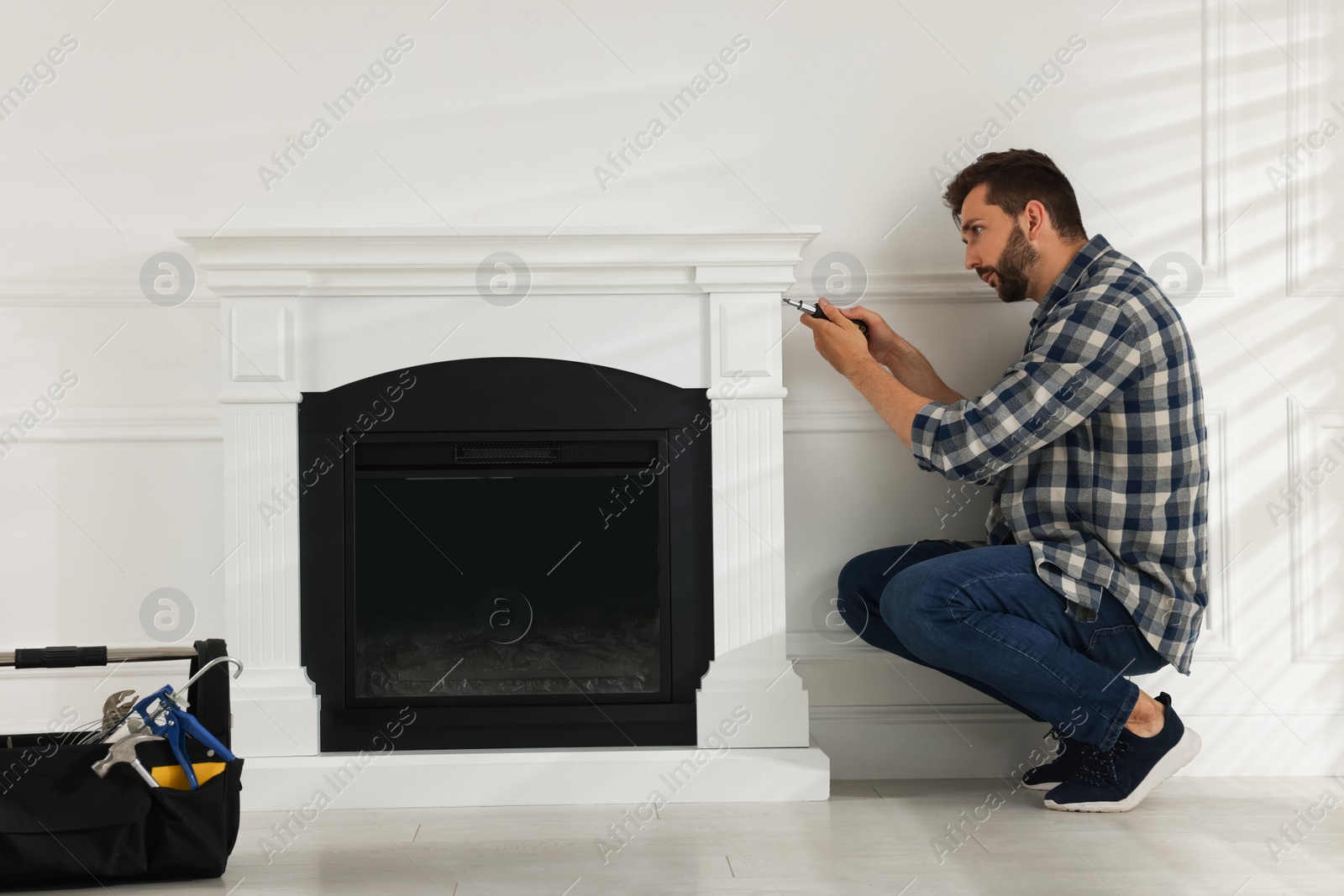 Photo of Man with screwdriver installing electric fireplace in room