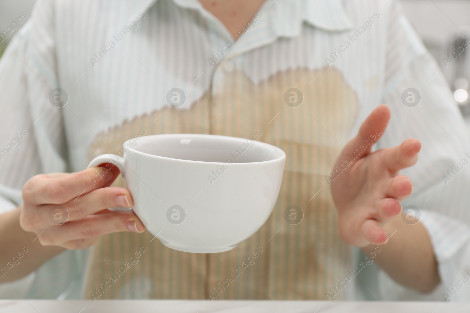 Photo of Woman with spilled coffee over her shirt at table, closeup