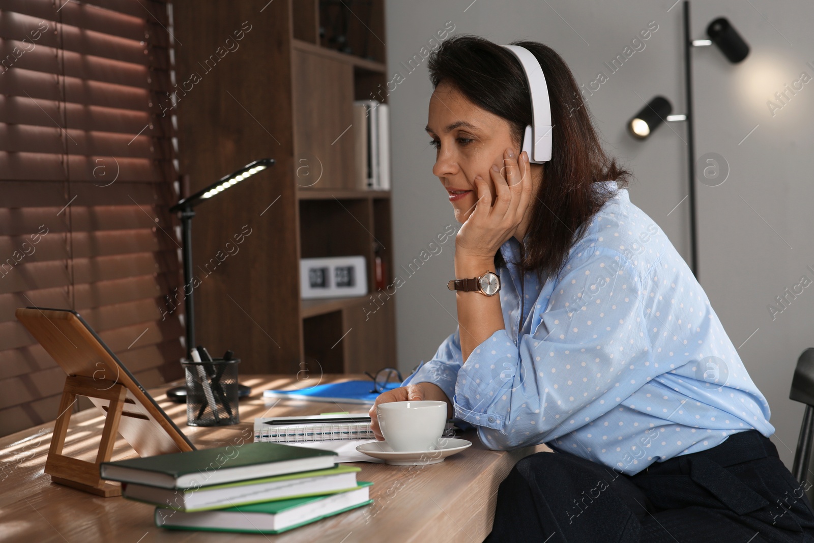 Photo of Woman with modern tablet and headphones learning at table indoors