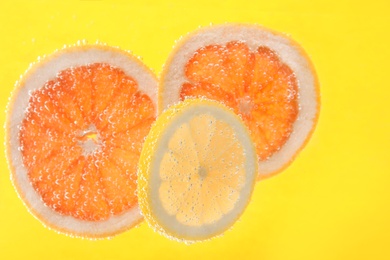 Slices of different citrus fruits in sparkling water on yellow background